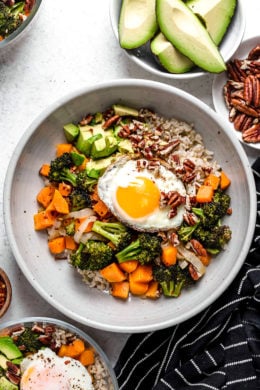 This easy Buddha Bowl is made with roasted broccoli, butternut squash, and onions piled on top of whole grain rice and topped with sliced avocado, a sunny-side fried egg, and crunchy pecans.