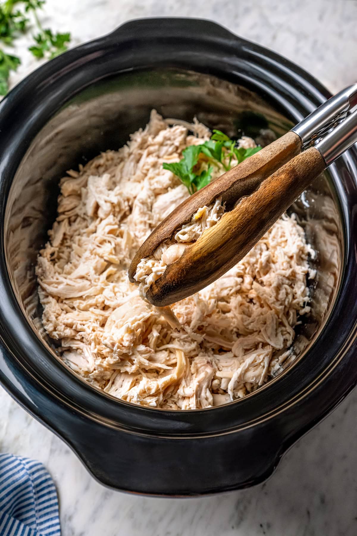 Tongs grabbing shredded chicken from slow cooker